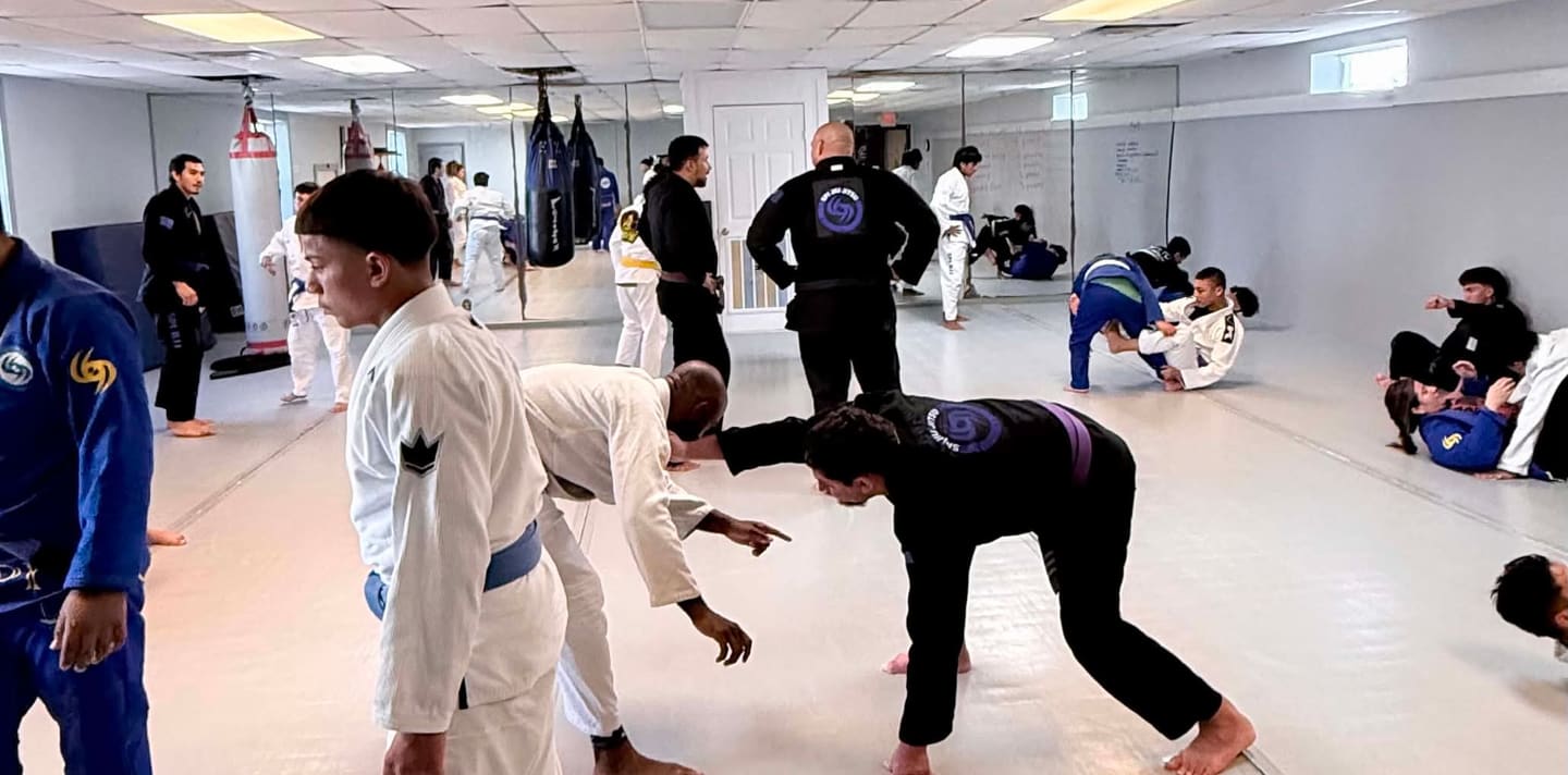 Adults drilling in gi on the mat during an evening class.