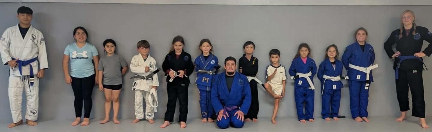 The SPI Jiu Jitsu kids class lined up across the mat with their coach.