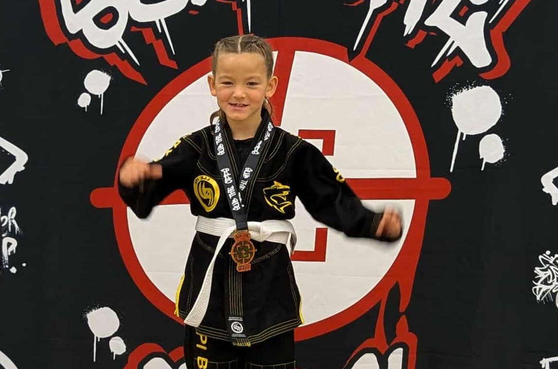 A young SPI Jiu Jitsu student on the top step of the podium at a tournament, wearing her medal.