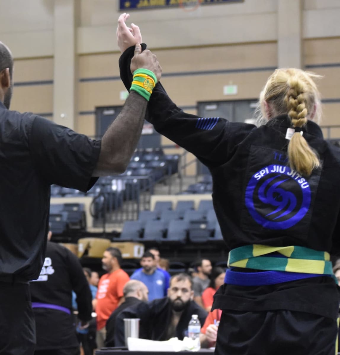 A SPI Jiu Jitsu competitor having her hand raised by the referee after winning her match at a tournament.